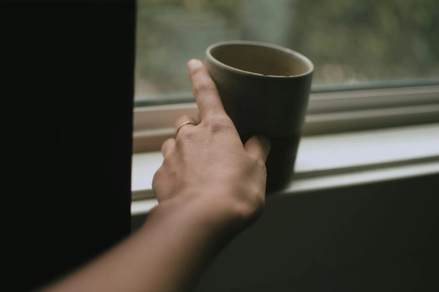 Una mano dejando una taza tibia sobre el alféizar de una ventana