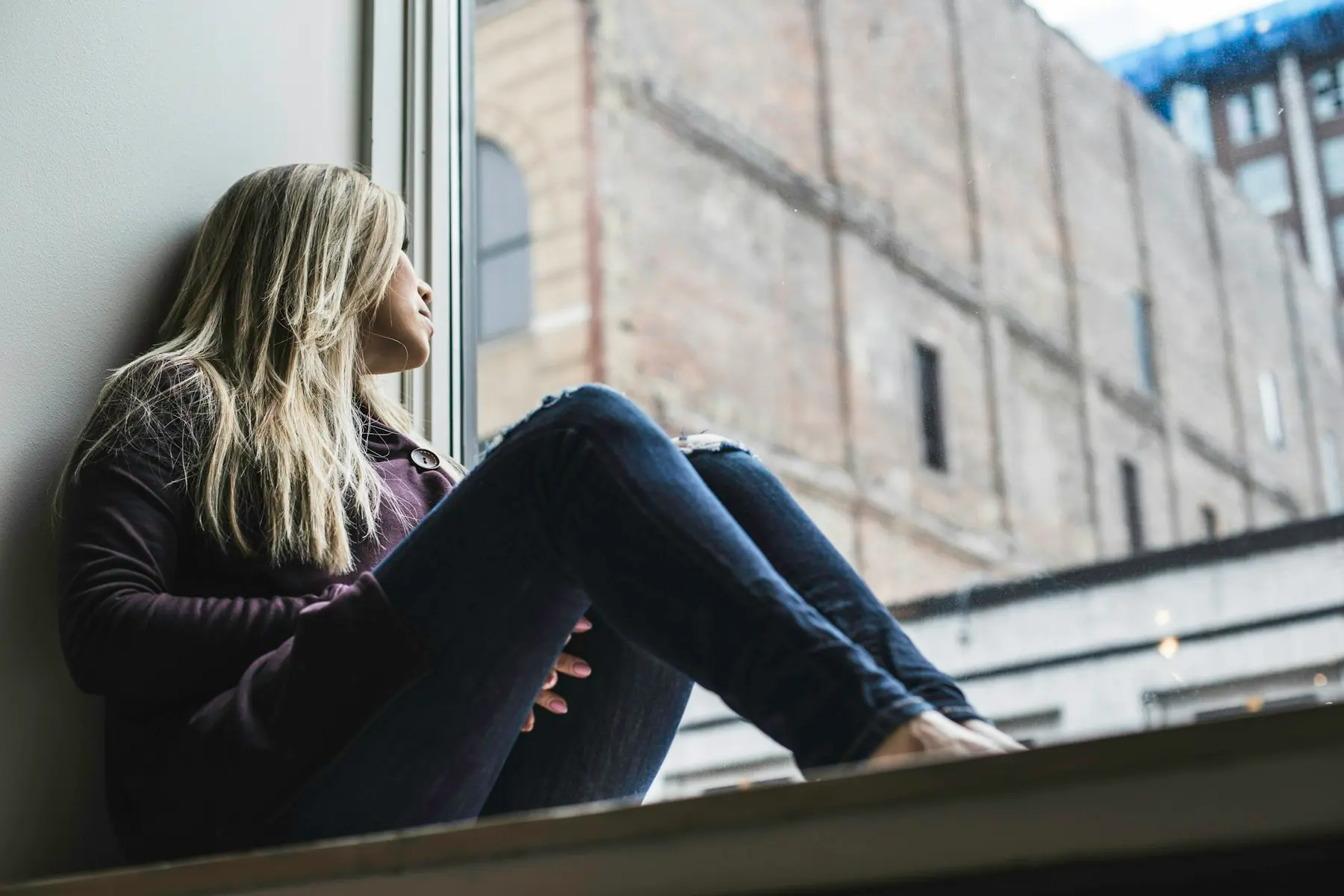 Una persona joven sentada en el alféizar de una ventana, mirando afuera